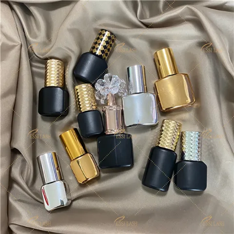 Assorted luxury eyelash extension adhesive bottles with gold and silver caps displayed on satin fabric, showcasing various lash glue packaging styles