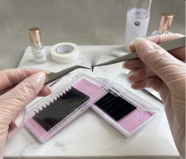 Hands in white gloves applying a volume lash fan.